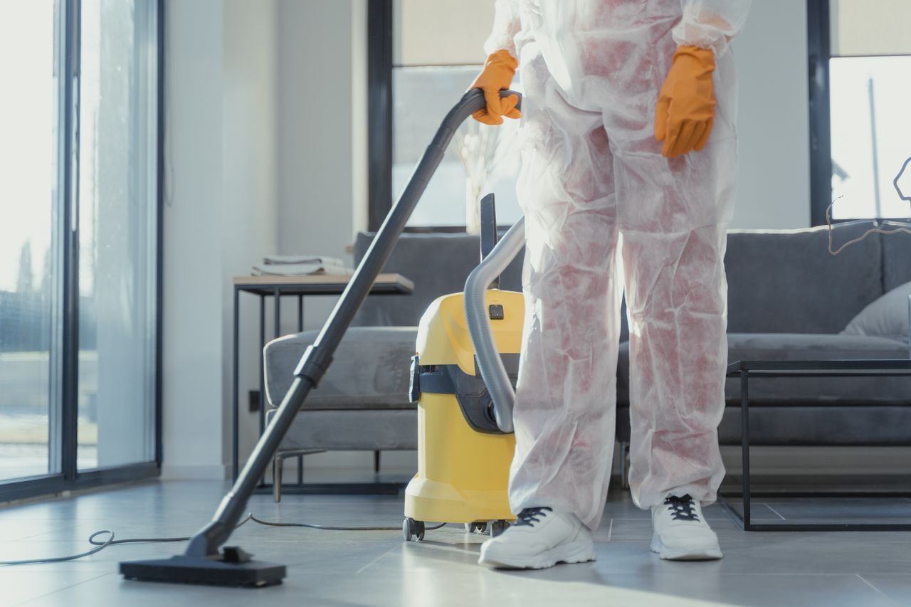 team-01 A cleaner in protective coveralls and gloves vacuuming a modern living room.